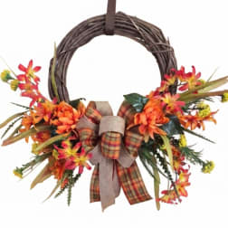 Fall wreath with orange flowers and a plaid bow on a grapevine ring