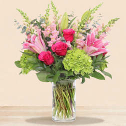 Pink lilies and roses with green hydrangea in a clear glass vase
