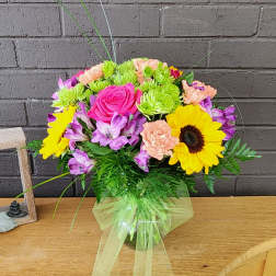 Mixed bouquet with pink roses, sunflowers, and purple flowers in a glass vase