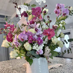 Tall arrangement of pink and purple orchids with white roses in a white ceramic vase
