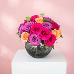 Bouquet of pink, purple, and peach roses in a round glass vase