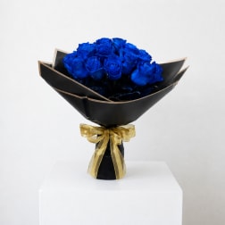 Bouquet of vivid blue roses wrapped in black paper with a gold ribbon