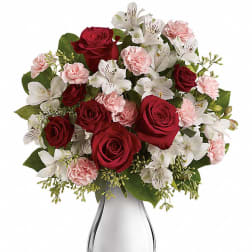 Arrangement of red roses, white alstroemeria, and light pink carnations in a shiny silver vase