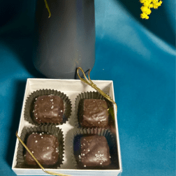 Yellow fluffy flowers in a dark vase beside a white box of four salted chocolate candies