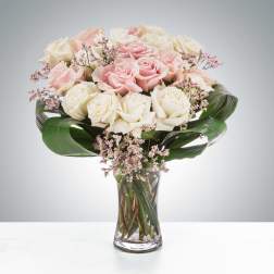 Pink and white roses arranged in a clear glass vase with broad green leaves