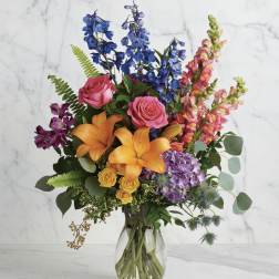 Colorful bouquet with roses, lilies, delphinium, and snapdragons in a glass vase