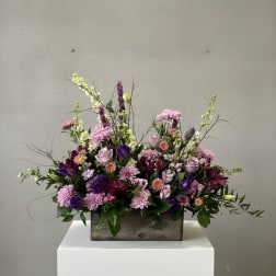 Mixed purple and pink flower arrangement in a wooden box