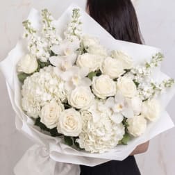 White bouquet of roses, orchids, and hydrangeas wrapped in paper