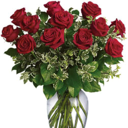 Red roses arranged in a clear glass vase with variegated greenery