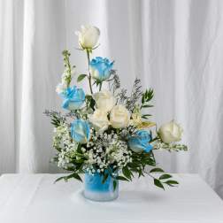 Blue and white roses arranged in a glass vase with greenery