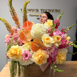 Large mixed flower arrangement in a woven basket with pink, yellow, and orange blooms