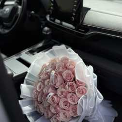 Bouquet of pale pink roses wrapped in white paper and ribbon on a car seat