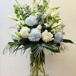 Tall white and pale blue floral arrangement in a glass vase