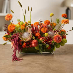 Low rectangular arrangement of orange and yellow flowers in a glass vase