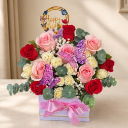 Pink and red roses arranged in a gift box with butterfly decorations and a birthday topper.