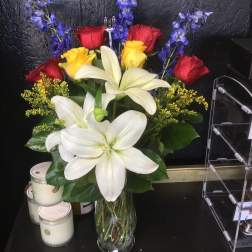 Bouquet of white lilies, red and yellow roses, and blue flowers in a glass vase