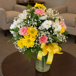 Mixed bouquet of daisies, carnations, and baby's breath in a glass vase with a yellow ribbon