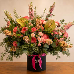 Large pink and peach floral arrangement in a black hatbox with a ribbon