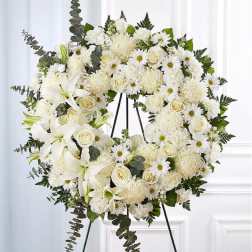 White floral wreath on a black easel with lilies, roses, and daisies
