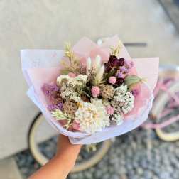 Handheld bouquet of pastel dried flowers wrapped in pink paper