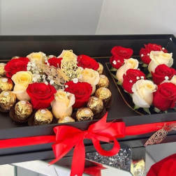 Boxed arrangement of red and cream roses with chocolates and a red ribbon
