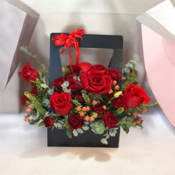 Red roses arranged in a black gift box with a red ribbon