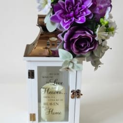 Purple and white floral arrangement on a white lantern with a candle inside
