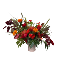 Mixed red and orange floral arrangement in a light vase