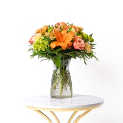 Orange and pink mixed bouquet in a clear glass vase on a table
