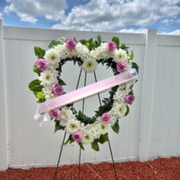 Heart-shaped floral wreath with pink roses and white flowers on an easel