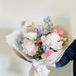 Hand-tied bouquet of pastel pink, white, and blue flowers wrapped in paper