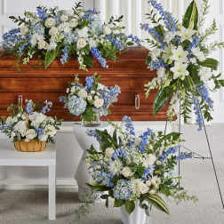 Blue and white floral funeral arrangements around a wooden casket