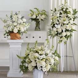 White floral arrangements with lilies and roses in baskets, vases, and a standing spray