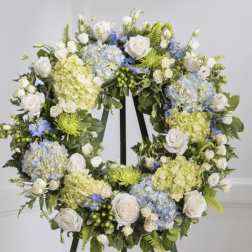 Floral wreath with white roses, blue hydrangeas, and pale green blooms on an easel