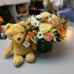 Teddy bear beside a mixed flower arrangement in a green vase