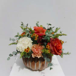 Orange and white floral arrangement in a pumpkin-shaped container