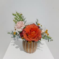 Orange rose arrangement in a ribbed ceramic vase with pink and yellow accents