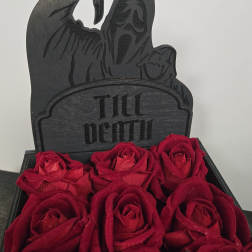 Red roses arranged below a black "Till Death" grave marker