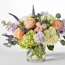 Bouquet of peach roses, hydrangeas, and purple flowers in a glass vase