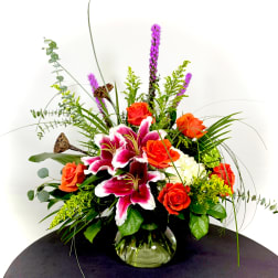 Orange roses and pink lilies in a glass vase with tall greenery