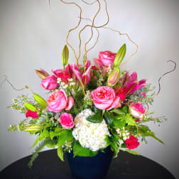 Pink roses and lilies arranged in a dark vase with white hydrangea