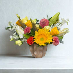 Mixed bouquet with sunflowers, roses, lilies, and pink blooms in a wooden vase