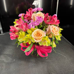 Mixed bouquet of peach roses, pink flowers, and yellow alstroemeria in a glass vase