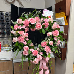 Pink rose and carnation wreath on a black stand with a pink ribbon