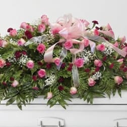 Pink rose casket spray with ribbon on a white casket
