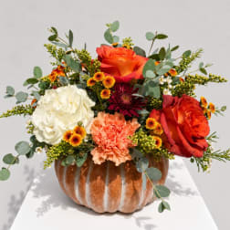 Mixed bouquet in a pumpkin-shaped vase with orange, white, and peach blooms