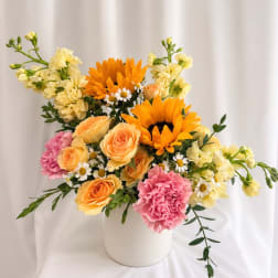 Mixed bouquet of sunflowers, roses, carnations, and small daisies in a white vase