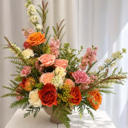 Mixed bouquet of orange, pink, and white flowers in a beige vase