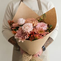 Handheld bouquet of pink and peach flowers wrapped in brown paper