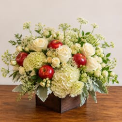 White roses and hydrangeas with red apples in a wooden box